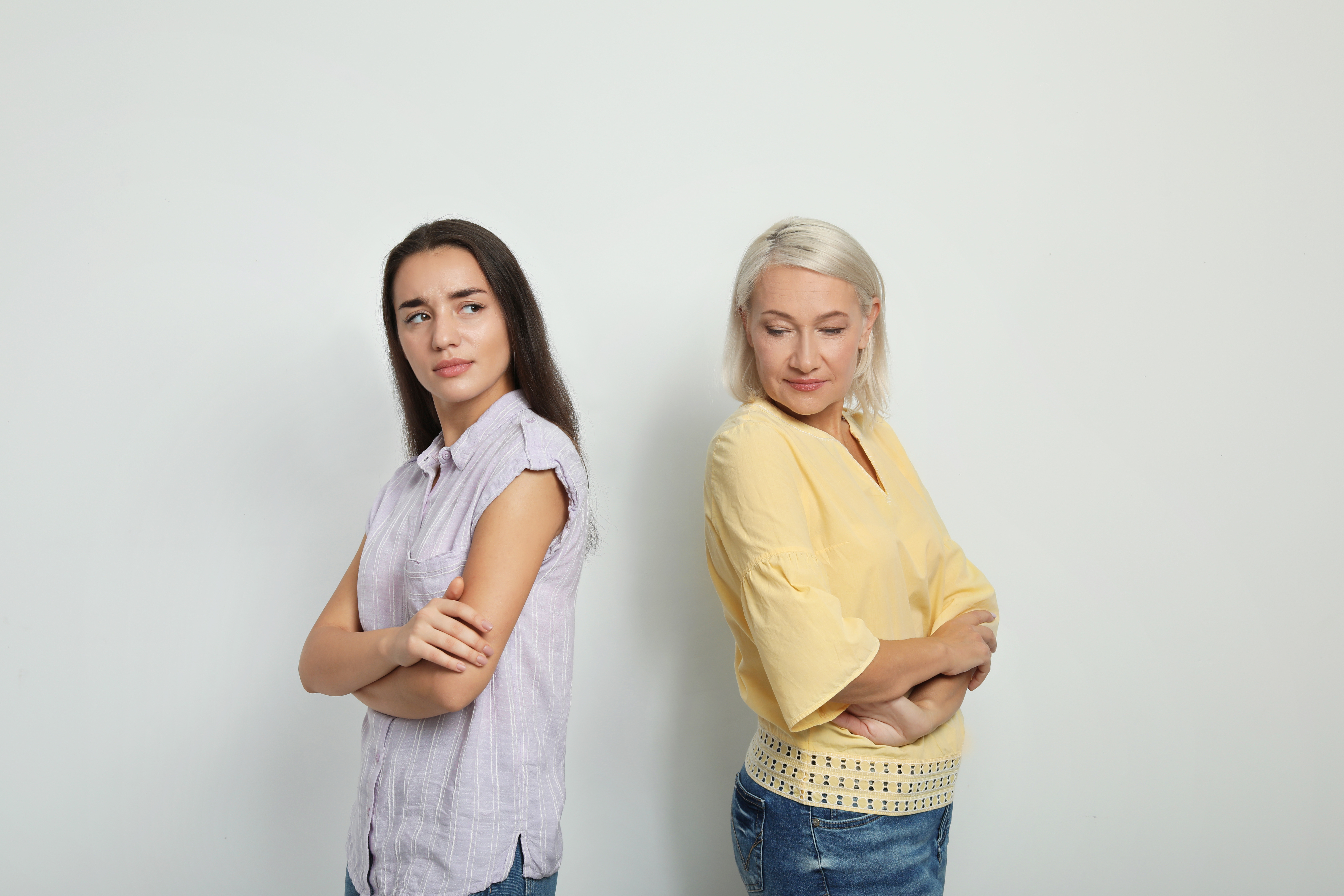 Portrait of young woman and her mother-in-law on white background. Family quarrel